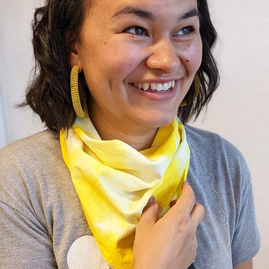 Jill smiles wearing a yellow tie dyed bandana and a friendship bracelet